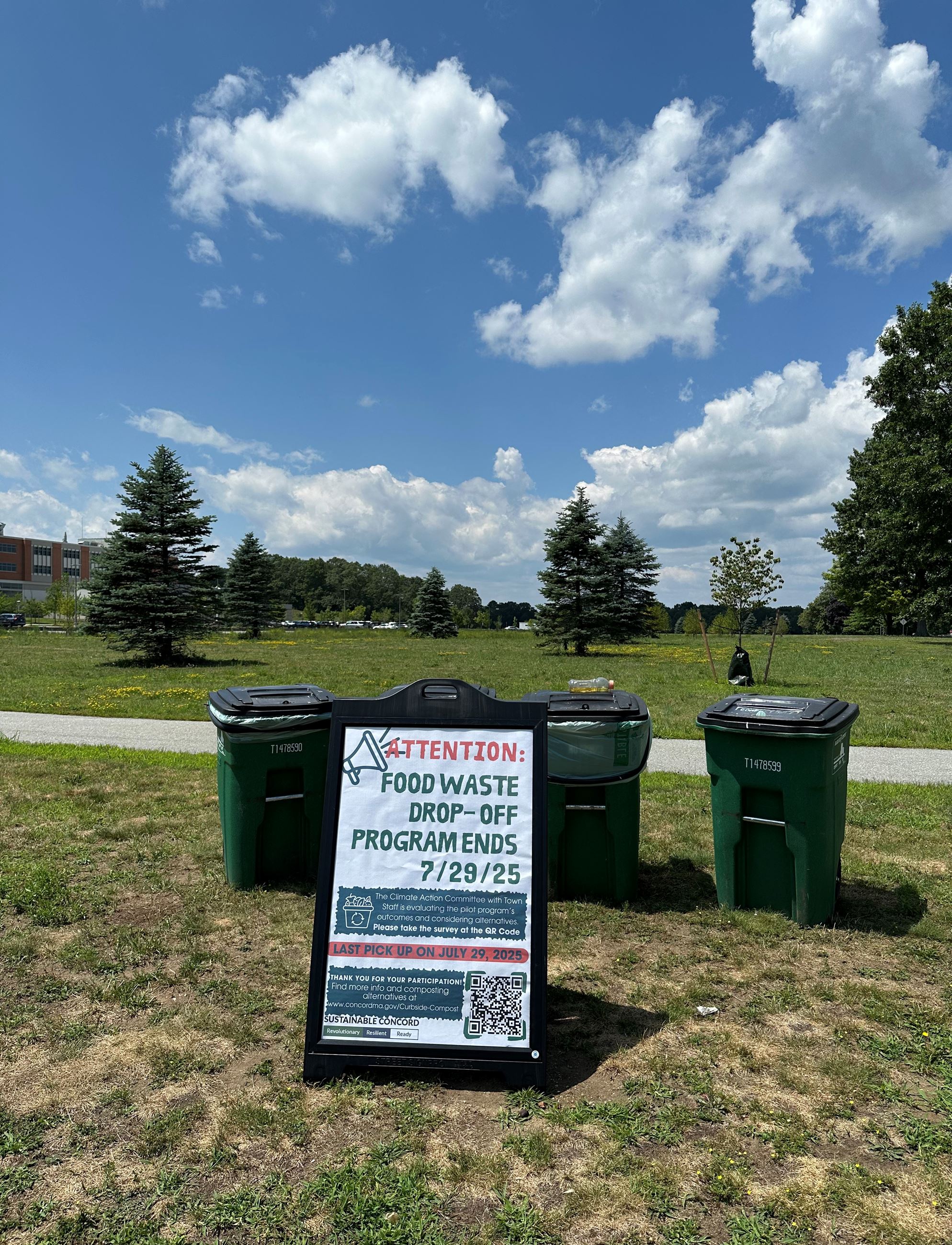 Sign board in front of barrels next to brick building - Food waster drop off ends 7/29/25